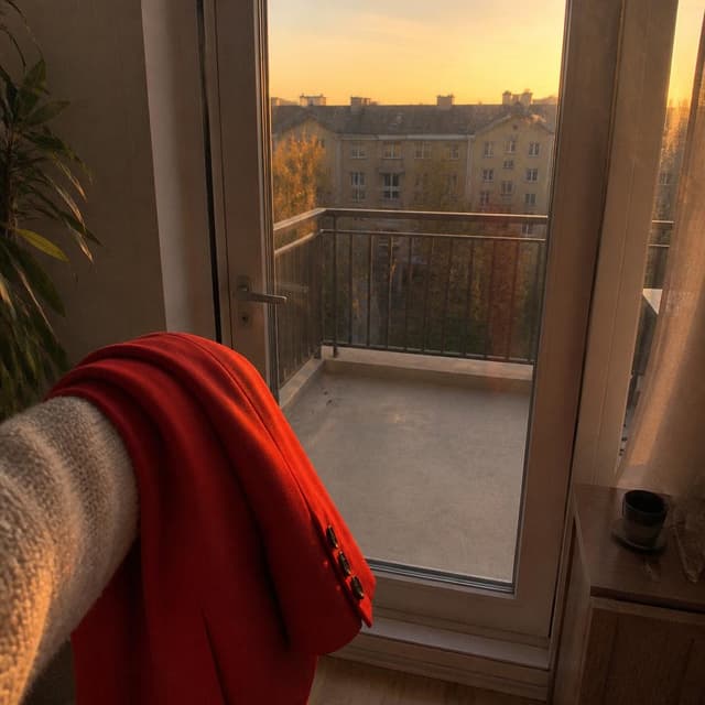 Charming ink and watercolor painting, clean lines, vibrant but soft color palette, storybook style. A phone-camera photo taken from inside a small apartment looking toward an empty balcony with the glass door now closed. A bright red women's jacket is folded over the arm of the person taking the photo — only their sleeve visible. Late-afternoon orange light through the glass. No other readable text
Chat attachment instruction: Generate exactly one in-world chat attachment, not a collage, split-screen, comic panel, flashback, or explanatory scene. If the prompt is a screenshot, phone screen, document, note, card, map, receipt, label, object photo, or photo someone took, frame that artifact directly. A name appearing in visible text or in 'photo taken by X' is not an instruction to draw that person. Do not show recurring story participants as visible people unless the prompt itself explicitly says they are visible. Keep unrequested people, faces, and bodies out of the image.