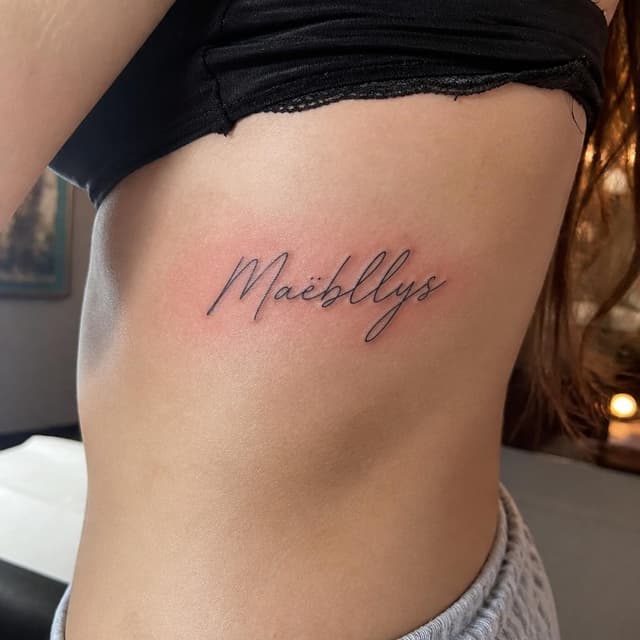 Charming ink and watercolor painting, storybook style. A close-up phone photo of fresh cursive script tattooed on a young woman's ribs, skin still slightly red. Visible text: "Maëllys". No other readable text
Chat attachment instruction: Generate exactly one in-world chat attachment, not a collage, split-screen, comic panel, flashback, or explanatory scene. If the prompt is a screenshot, phone screen, document, note, card, map, receipt, label, object photo, or photo someone took, frame that artifact directly. A name appearing in visible text or in 'photo taken by X' is not an instruction to draw that person. Do not show recurring story participants as visible people unless the prompt itself explicitly says they are visible. Keep unrequested people, faces, and bodies out of the image.