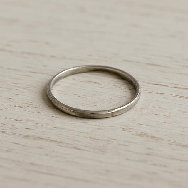 A thin old silver ring on a pale wooden surface
Chat attachment instruction: Generate exactly one in-world chat attachment, not a collage, split-screen, comic panel, flashback, or explanatory scene. If the prompt is a screenshot, phone screen, document, note, card, map, receipt, label, object photo, or photo someone took, frame that artifact directly. A name appearing in visible text or in 'photo taken by X' is not an instruction to draw that person. Do not show recurring story participants as visible people unless the prompt itself explicitly says they are visible. Keep unrequested people, faces, and bodies out of the image.