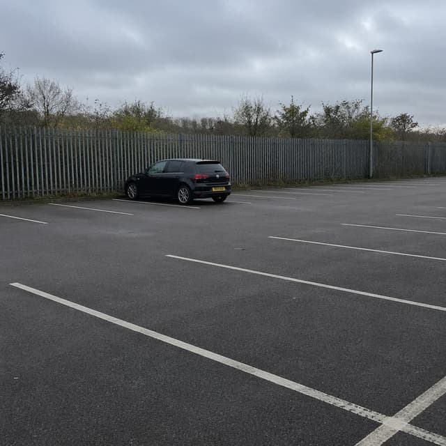 a lone dark-coloured car parked alone in an otherwise empty outdoor car park beside a metal fence
Chat attachment instruction: Generate exactly one in-world chat attachment, not a collage, split-screen, comic panel, flashback, or explanatory scene. If the prompt is a screenshot, phone screen, document, note, card, map, receipt, label, object photo, or photo someone took, frame that artifact directly. A name appearing in visible text or in 'photo taken by X' is not an instruction to draw that person. Do not show recurring story participants as visible people unless the prompt itself explicitly says they are visible. Keep unrequested people, faces, and bodies out of the image.
