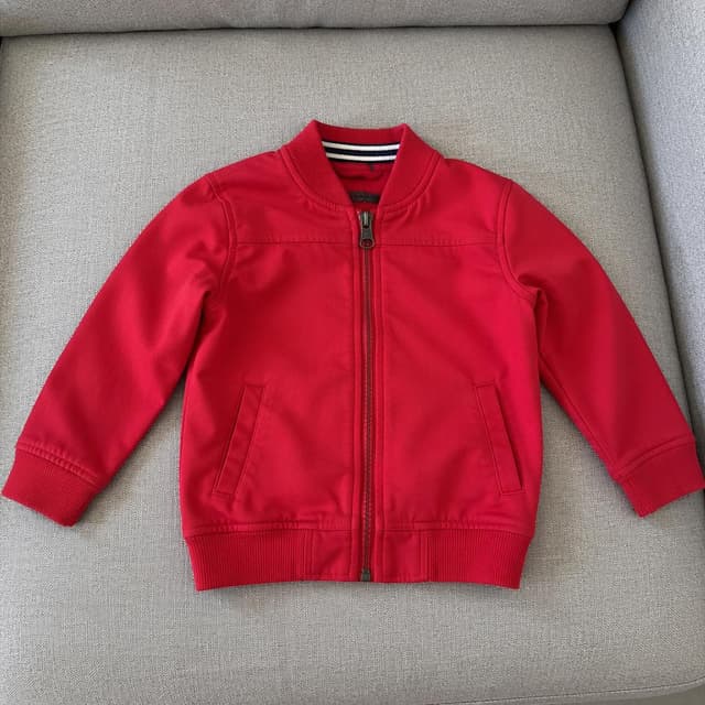 A small child's red zip-up jacket lying flat on a light grey sofa cushion
Chat attachment instruction: Generate exactly one in-world chat attachment, not a collage, split-screen, comic panel, flashback, or explanatory scene. If the prompt is a screenshot, phone screen, document, note, card, map, receipt, label, object photo, or photo someone took, frame that artifact directly. A name appearing in visible text or in 'photo taken by X' is not an instruction to draw that person. Do not show recurring story participants as visible people unless the prompt itself explicitly says they are visible. Keep unrequested people, faces, and bodies out of the image.