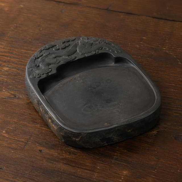 An old ink stone resting on a plain wooden writing desk surface
Chat attachment instruction: Generate exactly one in-world chat attachment, not a collage, split-screen, comic panel, flashback, or explanatory scene. If the prompt is a screenshot, phone screen, document, note, card, map, receipt, label, object photo, or photo someone took, frame that artifact directly. A name appearing in visible text or in 'photo taken by X' is not an instruction to draw that person. Do not show recurring story participants as visible people unless the prompt itself explicitly says they are visible. Keep unrequested people, faces, and bodies out of the image.