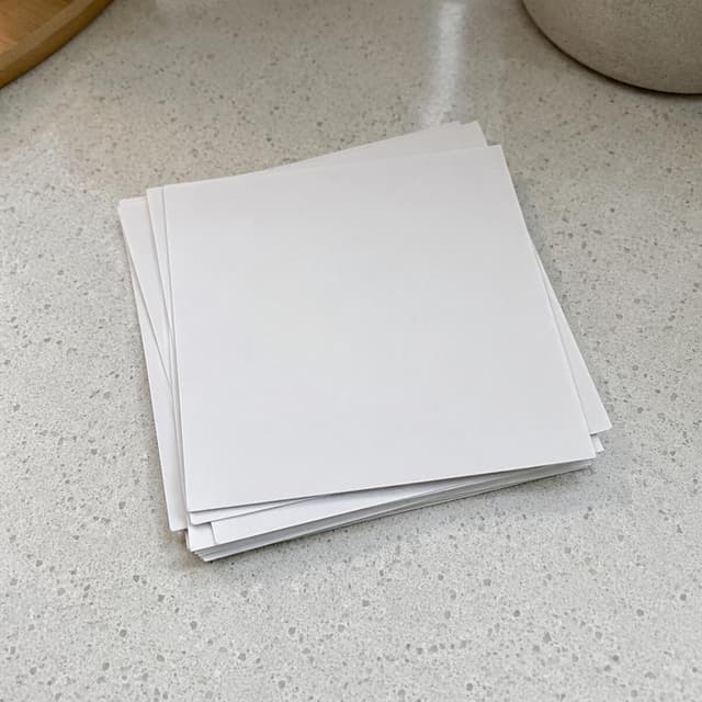A small pile of blank white photographs lying face-down on a pale kitchen counter, edges slightly uneven
Chat attachment instruction: Generate exactly one in-world chat attachment, not a collage, split-screen, comic panel, flashback, or explanatory scene. If the prompt is a screenshot, phone screen, document, note, card, map, receipt, label, object photo, or photo someone took, frame that artifact directly. A name appearing in visible text or in 'photo taken by X' is not an instruction to draw that person. Do not show recurring story participants as visible people unless the prompt itself explicitly says they are visible. Keep unrequested people, faces, and bodies out of the image.