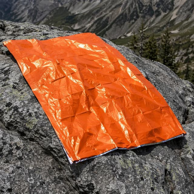 An orange rescue blanket spread over a grey mountain rock
Chat attachment instruction: Generate exactly one in-world chat attachment, not a collage, split-screen, comic panel, flashback, or explanatory scene. If the prompt is a screenshot, phone screen, document, note, card, map, receipt, label, object photo, or photo someone took, frame that artifact directly. A name appearing in visible text or in 'photo taken by X' is not an instruction to draw that person. Do not show recurring story participants as visible people unless the prompt itself explicitly says they are visible. Keep unrequested people, faces, and bodies out of the image.