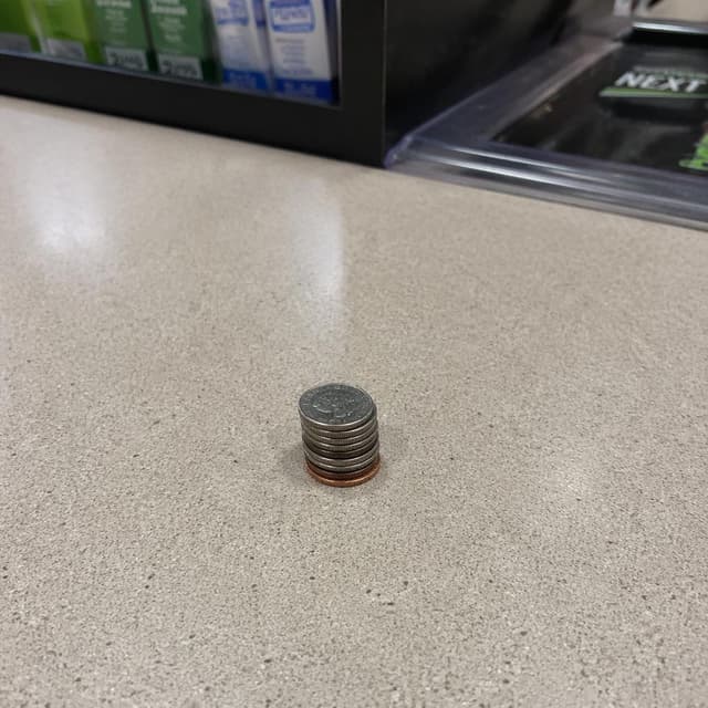 A small, neat stack of coins arranged precisely on a bare convenience store counter
Chat attachment instruction: Generate exactly one in-world chat attachment, not a collage, split-screen, comic panel, flashback, or explanatory scene. If the prompt is a screenshot, phone screen, document, note, card, map, receipt, label, object photo, or photo someone took, frame that artifact directly. A name appearing in visible text or in 'photo taken by X' is not an instruction to draw that person. Do not show recurring story participants as visible people unless the prompt itself explicitly says they are visible. Keep unrequested people, faces, and bodies out of the image.