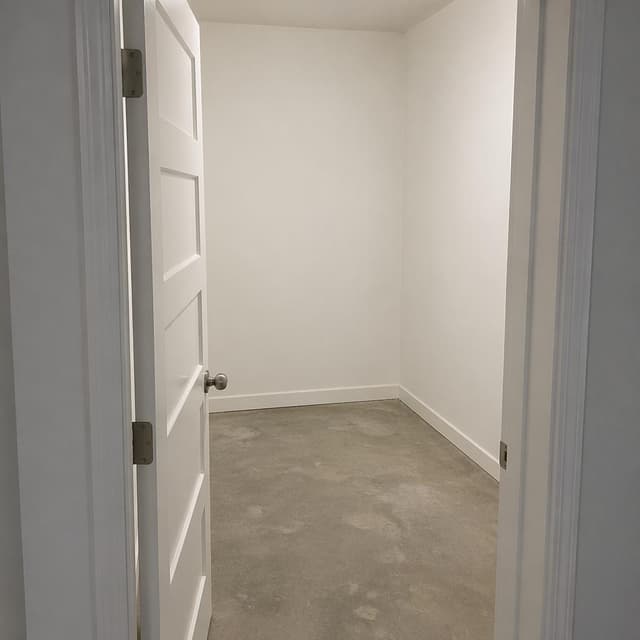 An open door leading into a small, empty, bare room with plain white walls
Chat attachment instruction: Generate exactly one in-world chat attachment, not a collage, split-screen, comic panel, flashback, or explanatory scene. If the prompt is a screenshot, phone screen, document, note, card, map, receipt, label, object photo, or photo someone took, frame that artifact directly. A name appearing in visible text or in 'photo taken by X' is not an instruction to draw that person. Do not show recurring story participants as visible people unless the prompt itself explicitly says they are visible. Keep unrequested people, faces, and bodies out of the image.