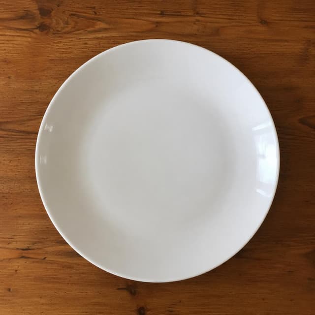 A close-up photo taken from a first-person perspective looking down at an empty white ceramic plate on a wooden kitchen table
Chat attachment instruction: Generate exactly one in-world chat attachment, not a collage, split-screen, comic panel, flashback, or explanatory scene. If the prompt is a screenshot, phone screen, document, note, card, map, receipt, label, object photo, or photo someone took, frame that artifact directly. A name appearing in visible text or in 'photo taken by X' is not an instruction to draw that person. Do not show recurring story participants as visible people unless the prompt itself explicitly says they are visible. Keep unrequested people, faces, and bodies out of the image.