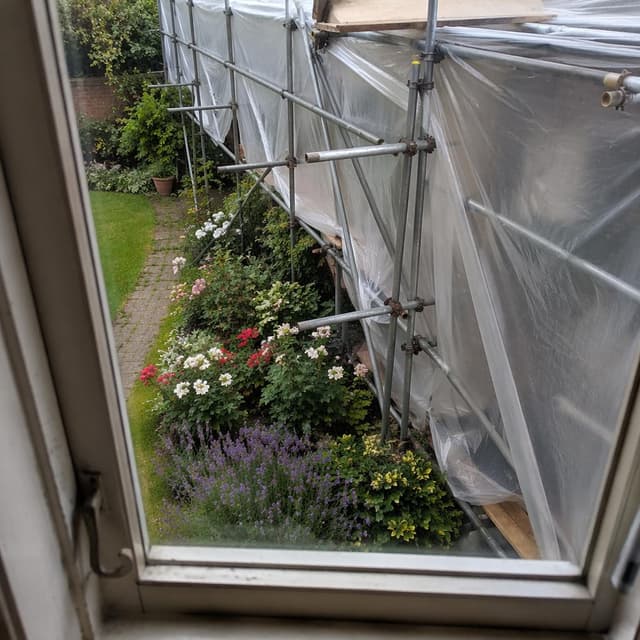 A view from a window looking down at a garden, showing a messy construction of metal pipes and plastic film encroaching on a flower bed
Chat attachment instruction: Generate exactly one in-world chat attachment, not a collage, split-screen, comic panel, flashback, or explanatory scene. If the prompt is a screenshot, phone screen, document, note, card, map, receipt, label, object photo, or photo someone took, frame that artifact directly. A name appearing in visible text or in 'photo taken by X' is not an instruction to draw that person. Do not show recurring story participants as visible people unless the prompt itself explicitly says they are visible. Keep unrequested people, faces, and bodies out of the image.