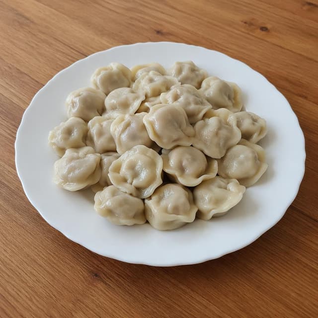 a white ceramic plate of steamed pelmeni on a plain wooden kitchen table
Chat attachment instruction: Generate exactly one in-world chat attachment, not a collage, split-screen, comic panel, flashback, or explanatory scene. If the prompt is a screenshot, phone screen, document, note, card, map, receipt, label, object photo, or photo someone took, frame that artifact directly. A name appearing in visible text or in 'photo taken by X' is not an instruction to draw that person. Do not show recurring story participants as visible people unless the prompt itself explicitly says they are visible. Keep unrequested people, faces, and bodies out of the image.