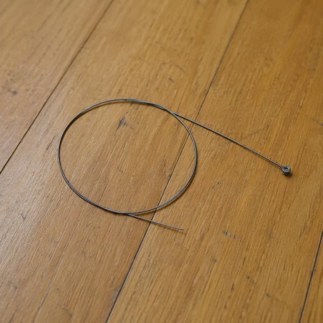 a single broken guitar string, coiled and snapped, lying on a plain wooden floor
Chat attachment instruction: Generate exactly one in-world chat attachment, not a collage, split-screen, comic panel, flashback, or explanatory scene. If the prompt is a screenshot, phone screen, document, note, card, map, receipt, label, object photo, or photo someone took, frame that artifact directly. A name appearing in visible text or in 'photo taken by X' is not an instruction to draw that person. Do not show recurring story participants as visible people unless the prompt itself explicitly says they are visible. Keep unrequested people, faces, and bodies out of the image.