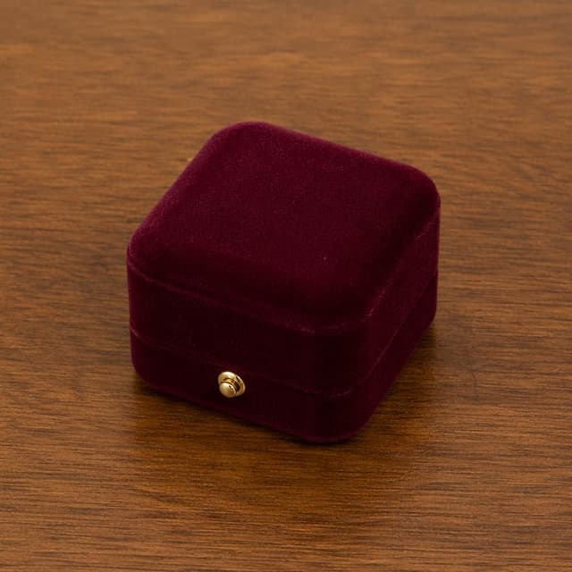 A small closed ring box on a plain wooden table
Chat attachment instruction: Generate exactly one in-world chat attachment, not a collage, split-screen, comic panel, flashback, or explanatory scene. If the prompt is a screenshot, phone screen, document, note, card, map, receipt, label, object photo, or photo someone took, frame that artifact directly. A name appearing in visible text or in 'photo taken by X' is not an instruction to draw that person. Do not show recurring story participants as visible people unless the prompt itself explicitly says they are visible. Keep unrequested people, faces, and bodies out of the image.