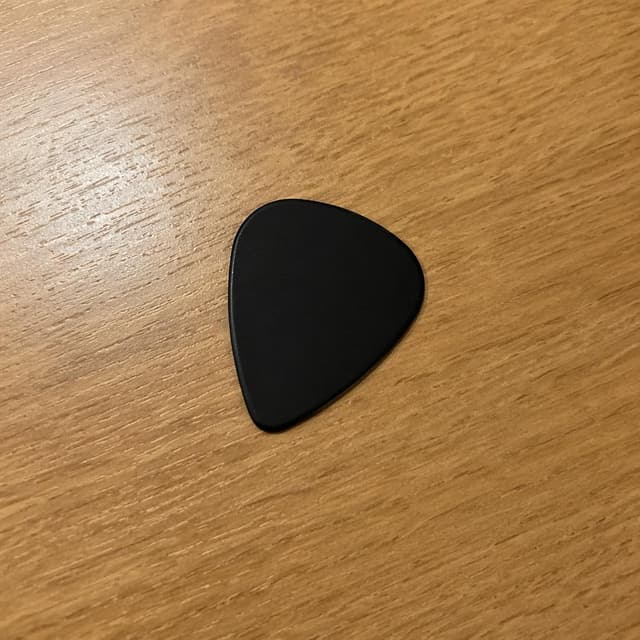 a single black guitar pick resting on a plain wooden desk
Chat attachment instruction: Generate exactly one in-world chat attachment, not a collage, split-screen, comic panel, flashback, or explanatory scene. If the prompt is a screenshot, phone screen, document, note, card, map, receipt, label, object photo, or photo someone took, frame that artifact directly. A name appearing in visible text or in 'photo taken by X' is not an instruction to draw that person. Do not show recurring story participants as visible people unless the prompt itself explicitly says they are visible. Keep unrequested people, faces, and bodies out of the image.