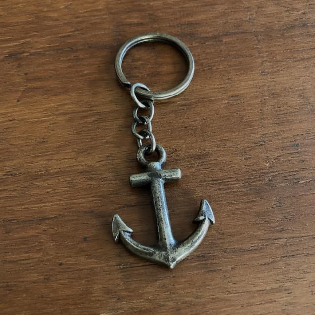 A small tarnished metal keychain shaped like an anchor on a plain wooden surface
Chat attachment instruction: Generate exactly one in-world chat attachment, not a collage, split-screen, comic panel, flashback, or explanatory scene. If the prompt is a screenshot, phone screen, document, note, card, map, receipt, label, object photo, or photo someone took, frame that artifact directly. A name appearing in visible text or in 'photo taken by X' is not an instruction to draw that person. Do not show recurring story participants as visible people unless the prompt itself explicitly says they are visible. Keep unrequested people, faces, and bodies out of the image.