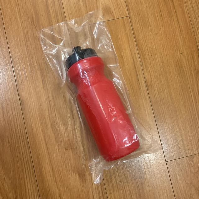 A red sports water bottle inside a clear plastic bag on a plain wooden floor
Chat attachment instruction: Generate exactly one in-world chat attachment, not a collage, split-screen, comic panel, flashback, or explanatory scene. If the prompt is a screenshot, phone screen, document, note, card, map, receipt, label, object photo, or photo someone took, frame that artifact directly. A name appearing in visible text or in 'photo taken by X' is not an instruction to draw that person. Do not show recurring story participants as visible people unless the prompt itself explicitly says they are visible. Keep unrequested people, faces, and bodies out of the image.