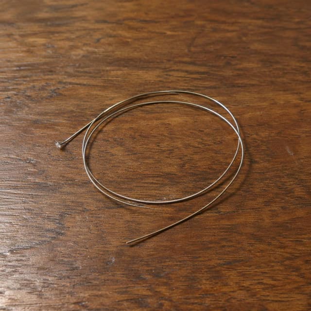 A single broken oud string, coiled loosely on a plain wooden table
Chat attachment instruction: Generate exactly one in-world chat attachment, not a collage, split-screen, comic panel, flashback, or explanatory scene. If the prompt is a screenshot, phone screen, document, note, card, map, receipt, label, object photo, or photo someone took, frame that artifact directly. A name appearing in visible text or in 'photo taken by X' is not an instruction to draw that person. Do not show recurring story participants as visible people unless the prompt itself explicitly says they are visible. Keep unrequested people, faces, and bodies out of the image.