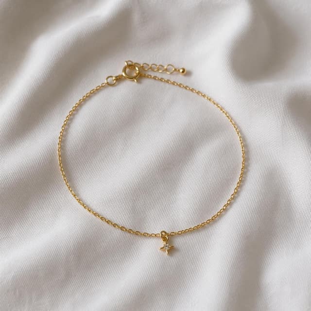 A small delicate gold bracelet with a tiny charm, resting on a plain white cloth
Chat attachment instruction: Generate exactly one in-world chat attachment, not a collage, split-screen, comic panel, flashback, or explanatory scene. If the prompt is a screenshot, phone screen, document, note, card, map, receipt, label, object photo, or photo someone took, frame that artifact directly. A name appearing in visible text or in 'photo taken by X' is not an instruction to draw that person. Do not show recurring story participants as visible people unless the prompt itself explicitly says they are visible. Keep unrequested people, faces, and bodies out of the image.