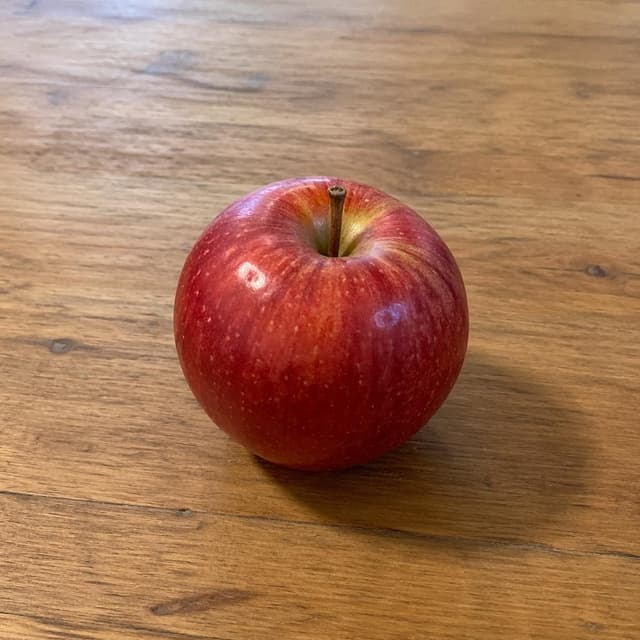 a single red apple on a plain wooden table
Chat attachment instruction: Generate exactly one in-world chat attachment, not a collage, split-screen, comic panel, flashback, or explanatory scene. If the prompt is a screenshot, phone screen, document, note, card, map, receipt, label, object photo, or photo someone took, frame that artifact directly. A name appearing in visible text or in 'photo taken by X' is not an instruction to draw that person. Do not show recurring story participants as visible people unless the prompt itself explicitly says they are visible. Keep unrequested people, faces, and bodies out of the image.