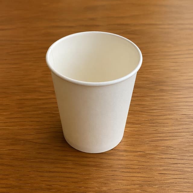 a single empty paper cup on a plain wooden table
Chat attachment instruction: Generate exactly one in-world chat attachment, not a collage, split-screen, comic panel, flashback, or explanatory scene. If the prompt is a screenshot, phone screen, document, note, card, map, receipt, label, object photo, or photo someone took, frame that artifact directly. A name appearing in visible text or in 'photo taken by X' is not an instruction to draw that person. Do not show recurring story participants as visible people unless the prompt itself explicitly says they are visible. Keep unrequested people, faces, and bodies out of the image.