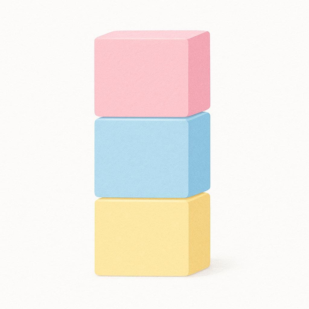 A collection of three simple, square blocks colored in very pale, soft pink, light blue, and pale yellow.