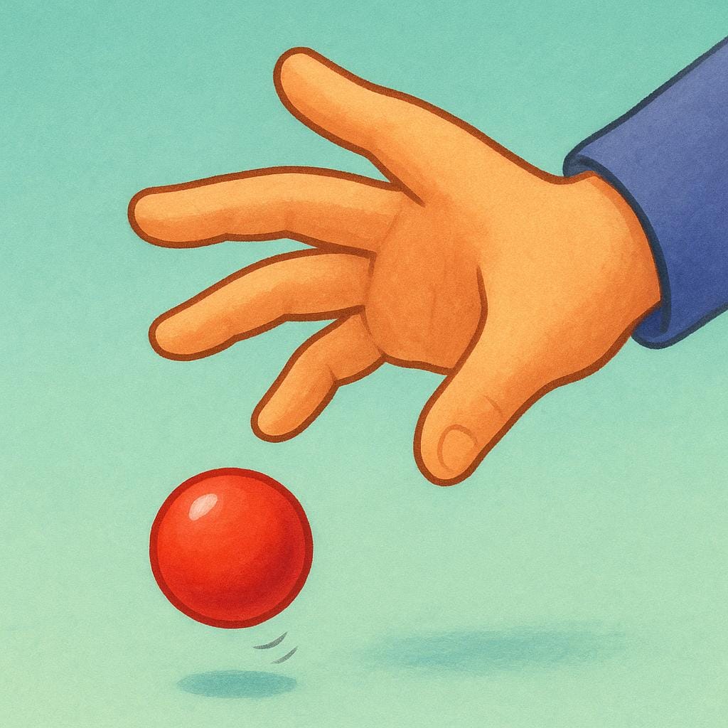 A close-up view of a person's hand opening its grip, allowing a small, colorful ball to fall downwards.