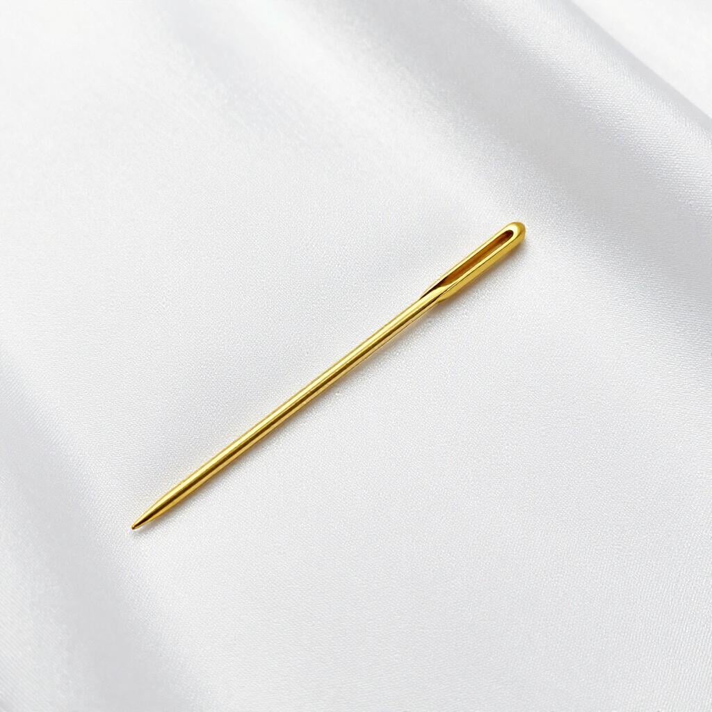 A very thin, delicate golden needle resting on a soft white fabric.