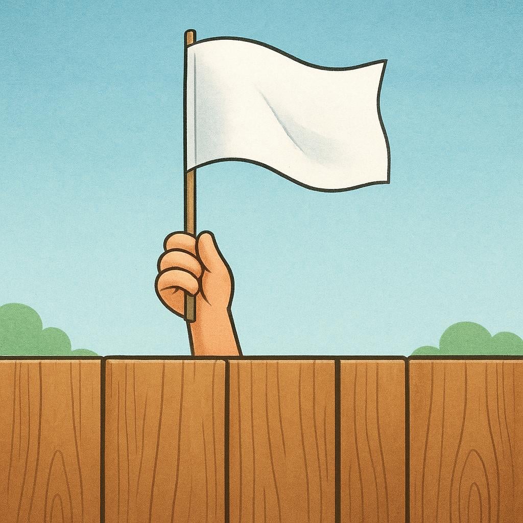 A small white flag being held up by a person's hand from behind a wooden fence.