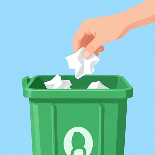 A person dropping a crumpled piece of paper into a small green trash can.