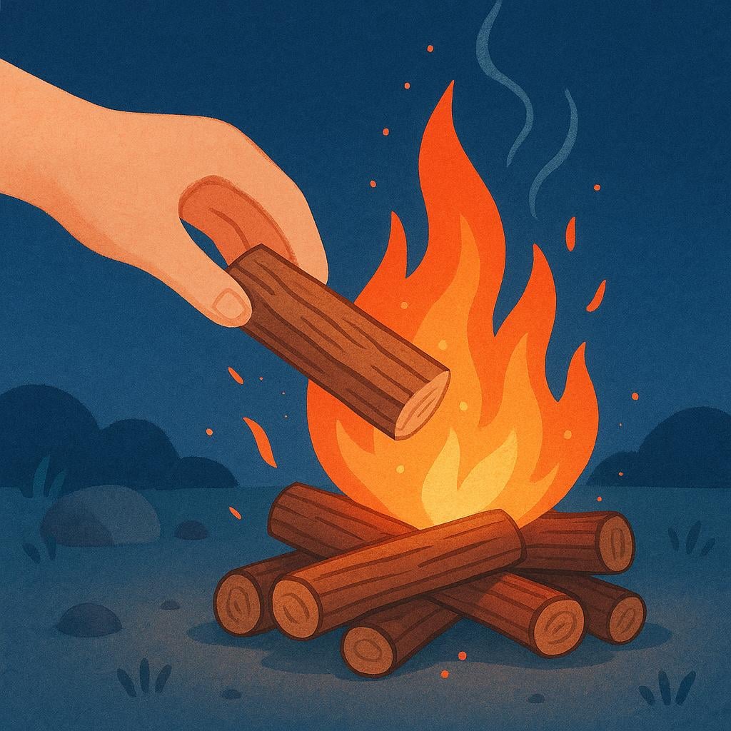 A close-up view of a hand carefully placing a piece of firewood onto a glowing campfire.