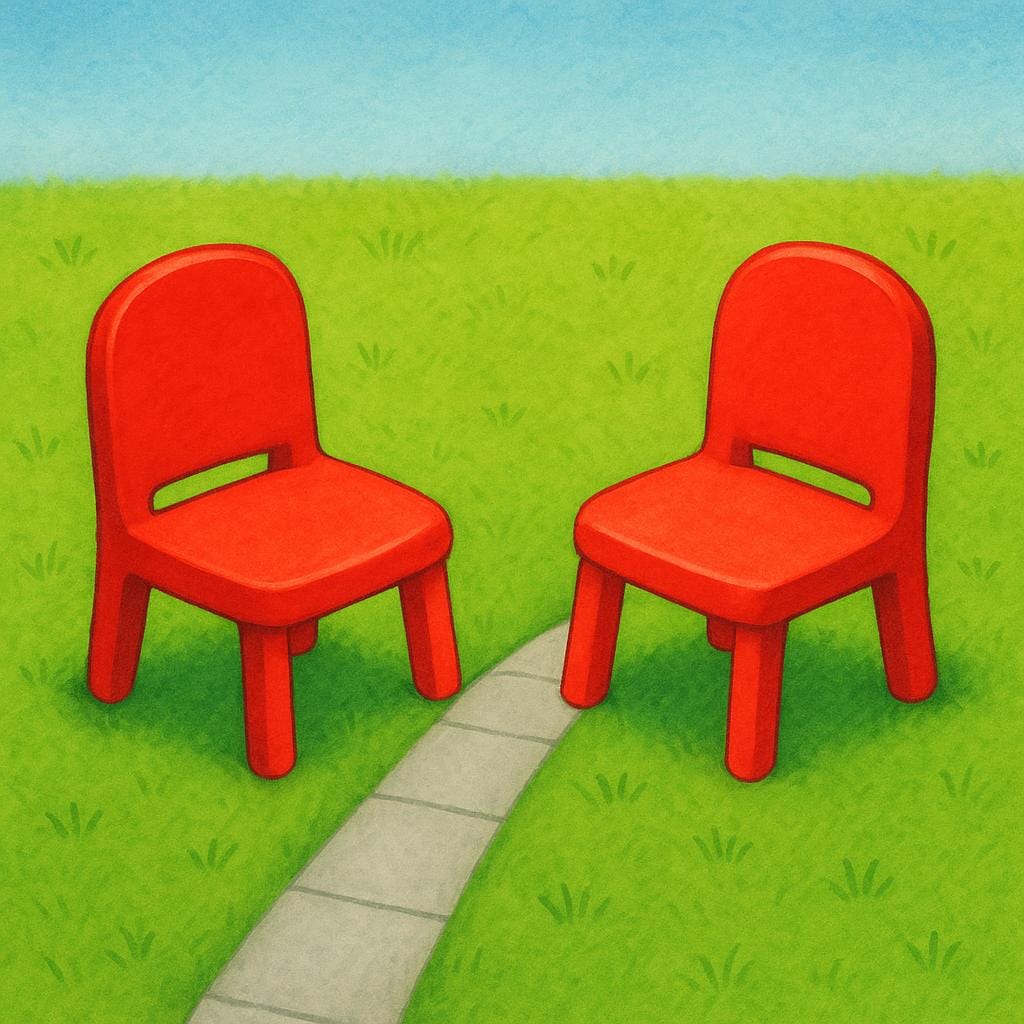 Two brightly colored red chairs are placed directly opposite each other on a green lawn, separated by a narrow paved path, illustrating the concept of being opposite or across the way.