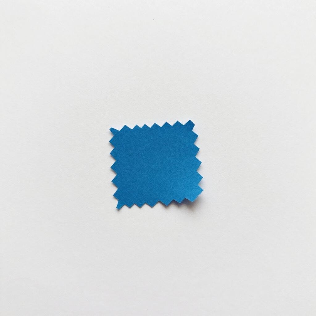 A single tiny blue scrap of paper on a clean white surface.