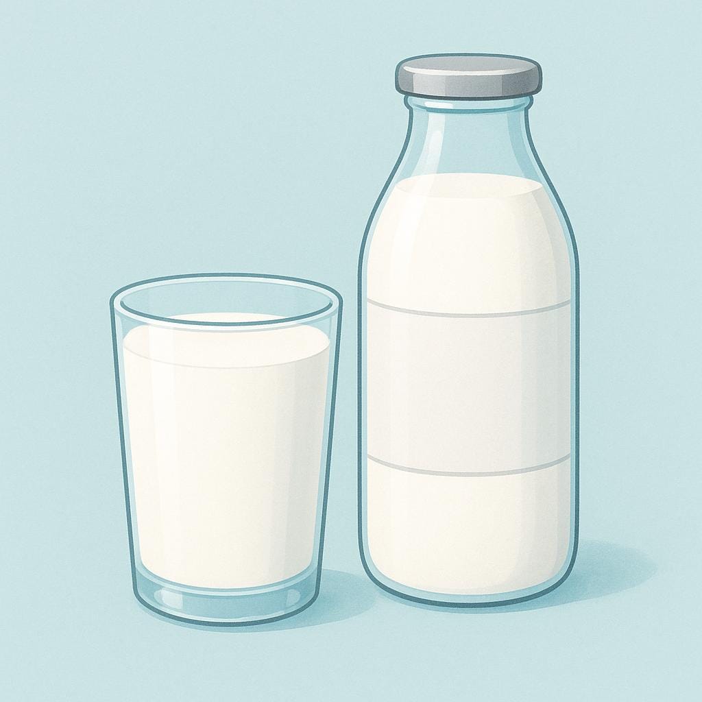 A tall, clear glass filled with white milk, sitting next to a traditional glass milk bottle with a silver foil cap.