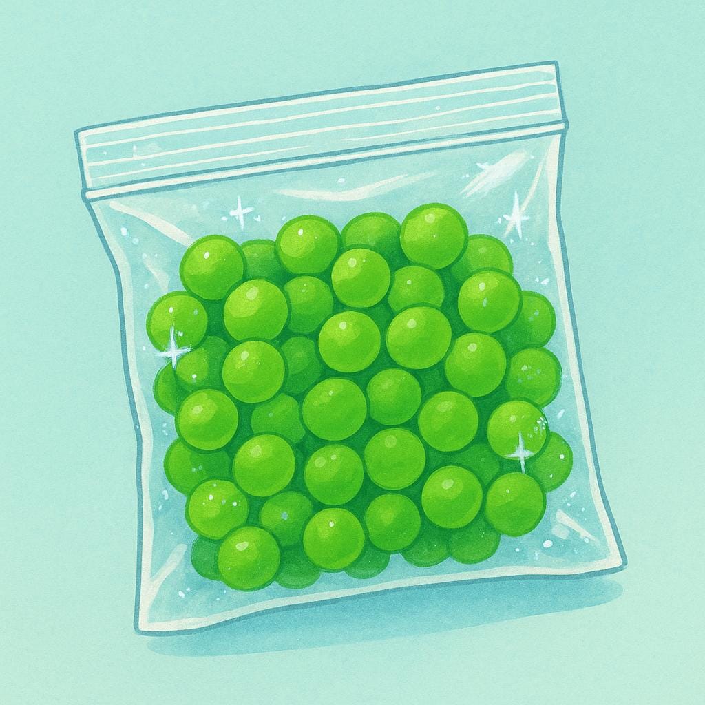 A colorful bag of frozen peas with a few loose green peas and small ice crystals around it.